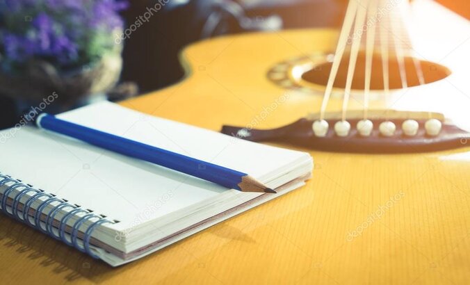 Songwriter writing lyrics in a notebook with a guitar beside them