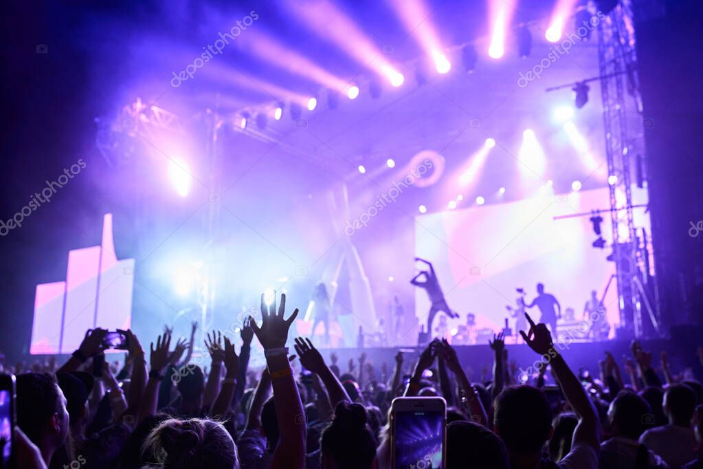 Crowd with hands up at a hip-hop concert with blue stage lights